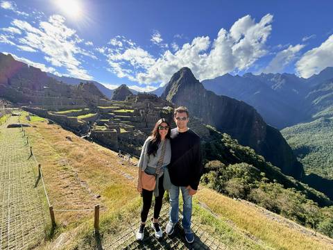 A couple poses at the classic postcard viewpoint overlooking Machu Picchu with jagged peaks behind.