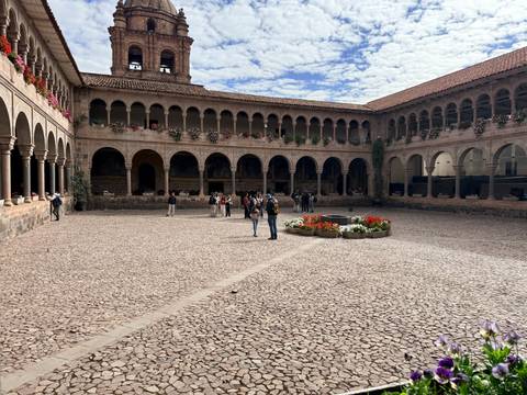 Visitors explore the cobblestone courtyard of Qorikancha monastery with arch colonnades in Cusco.