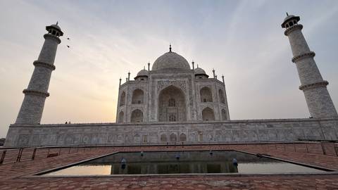 Silhouetted view of the Taj Mahal with soft sunset light behind its white marble façade.
