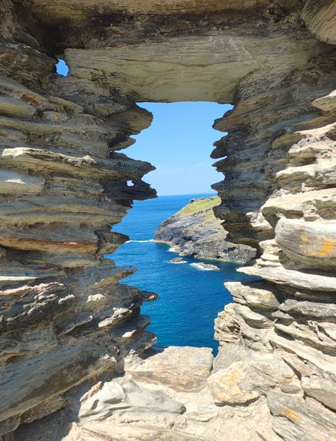 Dramatic coastal cliff view through a jagged rock window looking onto turquoise sea.