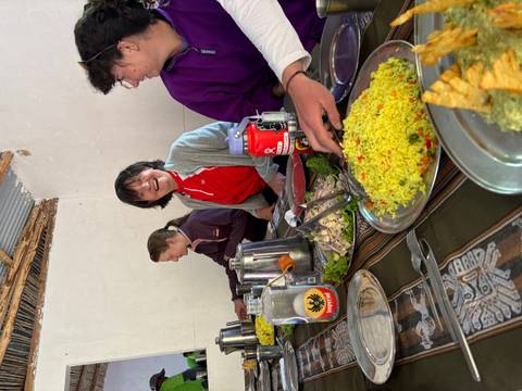 Travellers seated indoors enjoying a communal Peruvian meal with rice and salad dishes.