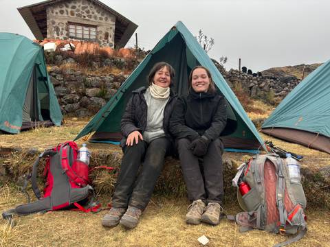 Two trekkers smiling in front of a green camping tent at an Andean campsite.