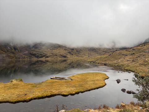 Mist-covered mountain lake with wooden raft and golden marsh grass peninsula.