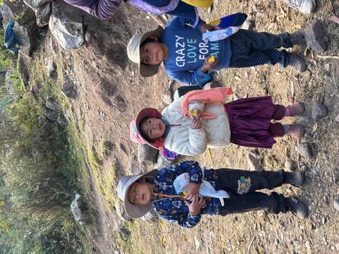 Three local children in rural Andean setting wearing colorful hats and sweaters.