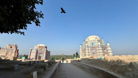Majestic mausoleum of Multan with bird flying overhead under bright blue sky.