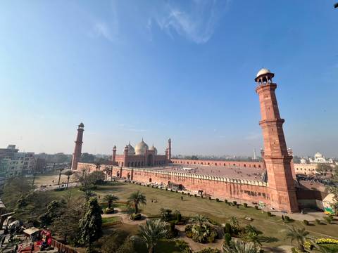Panoramic aerial view of Badshahi Mosque courtyard and minarets under blue sky.