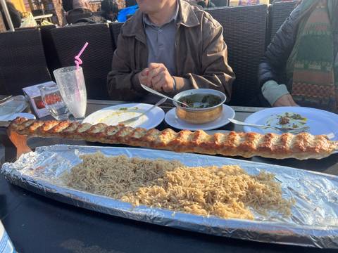 Pakistani kebab platter on long skewer served with rice at outdoor restaurant table.