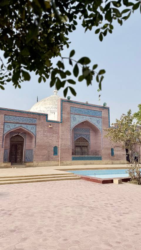 Side wall of Pakistani shrine with striped brickwork and decorative turquoise tiles.