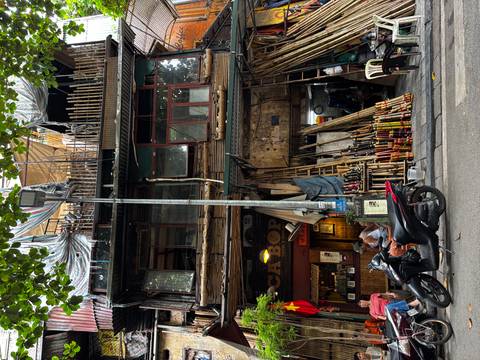 Rustic three-story bamboo-fronted shopfront with a scooter rider parked on a Hanoi street.