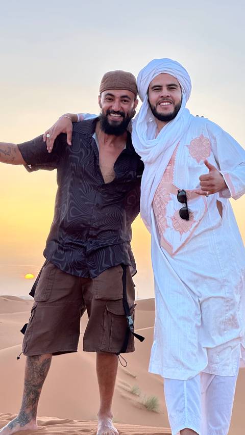 Close-crop of two friends in desert attire celebrating at sunset with golden sky behind.