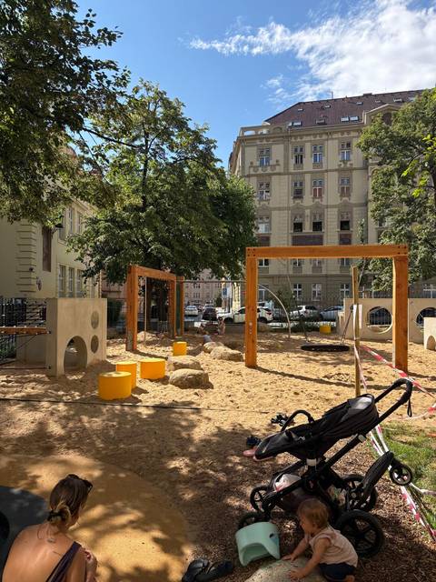 Urban playground with sand, climbing frames and a child playing surrounded by historic apartment buildings.