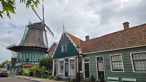 Traditional green wooden houses and a large historic windmill under a cloudy sky in Zaanse Schans.