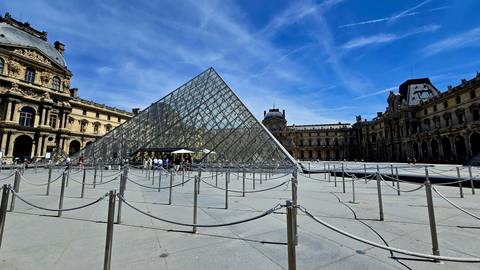 Wide shot of the Louvre Pyramid and surrounding palace buildings under a vivid blue sky.