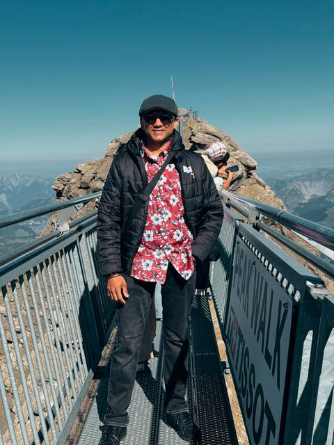 Traveller standing on a high alpine suspension bridge viewpoint with rugged Swiss peaks and a clear sky in the background.