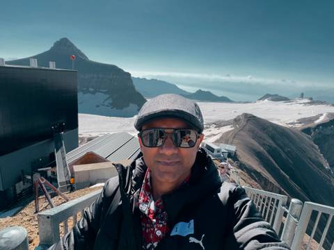 Traveller taking a selfie on a snowy mountain lookout with dramatic Swiss peaks and glaciers in the distance.