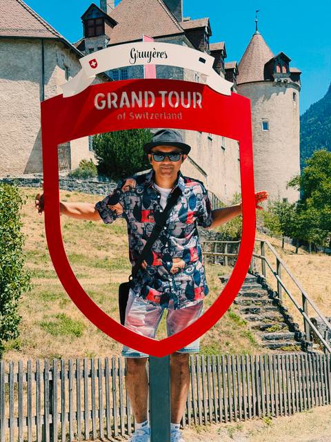 Traveller framed playfully within a large red shield sculpture in front of a Swiss castle.