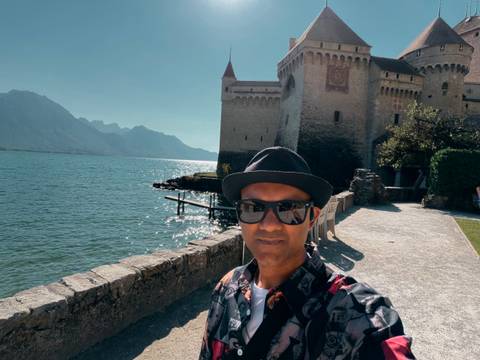 Self-portrait with the lakeside Château de Chillon and Alpine ridges in the background.
