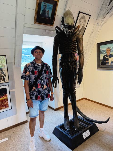 Visitor posing beside a tall, dark alien-themed sculpture inside the H. R. Giger Museum.