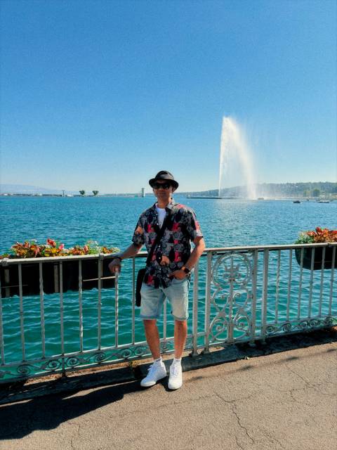 Traveller at Geneva’s lakeside railing with the Jet d’Eau fountain shooting water high into the sky.