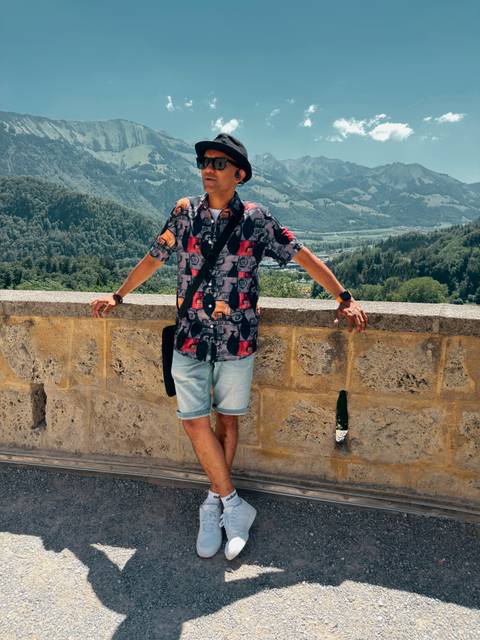 Traveller leaning casually on a stone wall with a lush green Swiss valley view below.