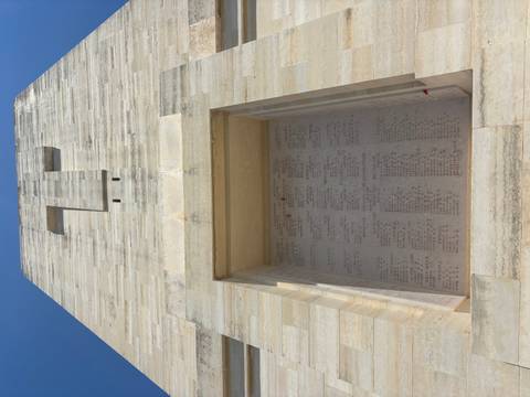 Upward view of a pale stone memorial wall engraved with soldiers’ names under a clear sky.