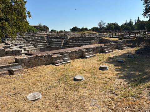 Stone remains of an ancient amphitheatre and surrounding ruins under late-afternoon light.