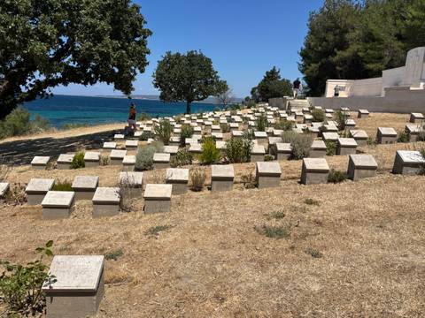 Rows of low stone grave markers overlook a bright blue sea at a coastal war cemetery.