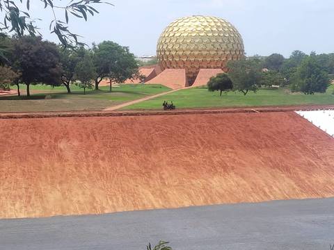 The golden geodesic Matrimandir sphere rises above manicured lawns and red earth pathways in Auroville.