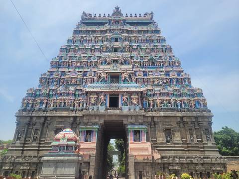 An intricately painted multicolour gopuram tower of a South Indian temple soars into the blue sky.