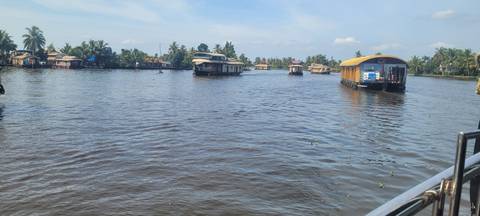 Traditional houseboats cruise the wide Kerala backwaters under a sunny blue sky.