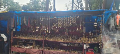 Outdoor stall displaying numerous brass souvenirs and trinkets under a blue tarpaulin.
