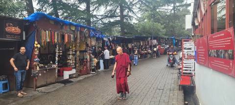 Pedestrian market street lined with souvenir stalls; a monk in red robes walks in the foreground.
