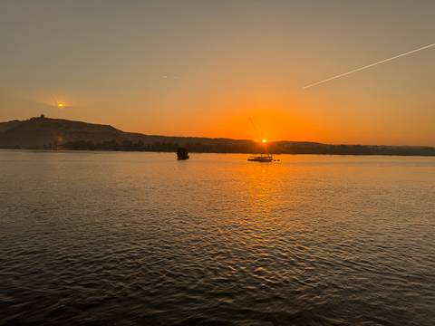 Orange sunset over the Nile with felucca sailboats and a silhouetted hill on the horizon.