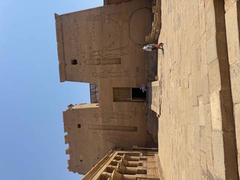 Massive sandstone pylon entrance of Edfu Temple with faint carved figures under bright sky.