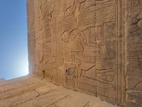 Relief carvings of pharaoh and deity on a tall temple wall lit by backlight.