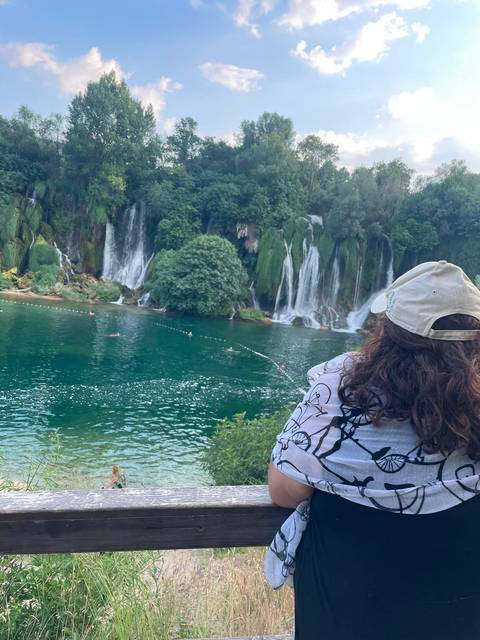 Visitor admiring multiple cascading waterfalls surrounded by lush greenery at a turquoise pool.