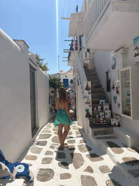 Back view of woman strolling through narrow whitewashed alley with stone steps and boutique displays