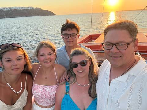 Family selfie on boat deck with calm sea and setting sun in background