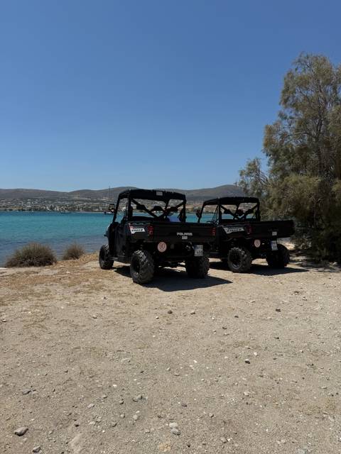 Two off-road Polaris utility vehicles parked beside turquoise bay under clear sky