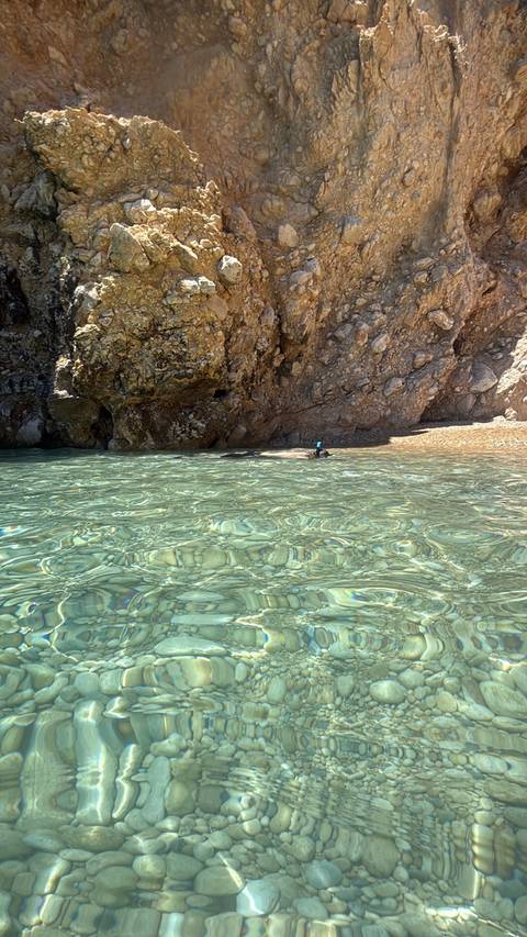 Snorkeller floating in crystal-clear shallow cove beneath rocky cliff face