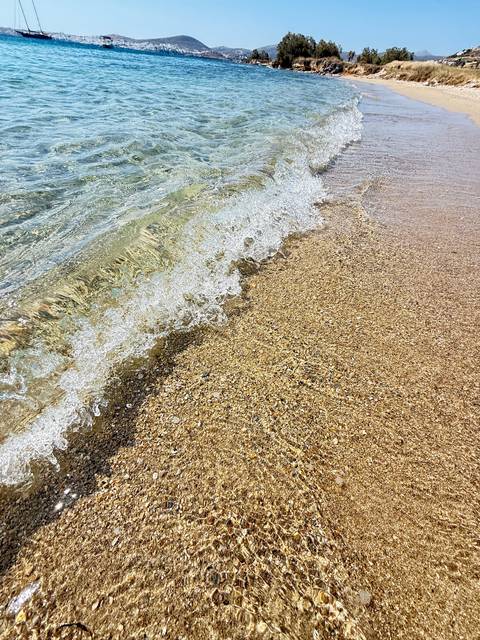Close-up of small wave washing over golden pebbly beach creating frothy pattern