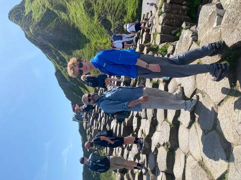 Travelers climb the basalt columns of the Giant’s Causeway under bright summer sun.