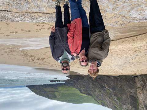 Family stands together on a windy sandy beach with cliffs and rolling waves behind.