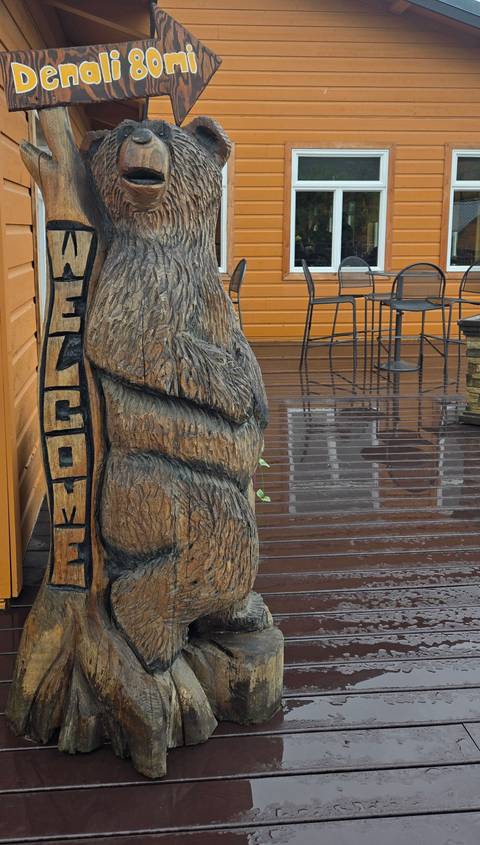 Close-cropped view of a carved wooden bear statue beside wet deck boards.