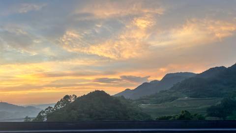 Soft pastel sunrise over layered green mountains and valleys in rural China.