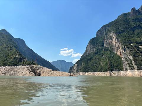 Steep green cliffs plunge into the wide Yangtze River beneath a clear blue sky.