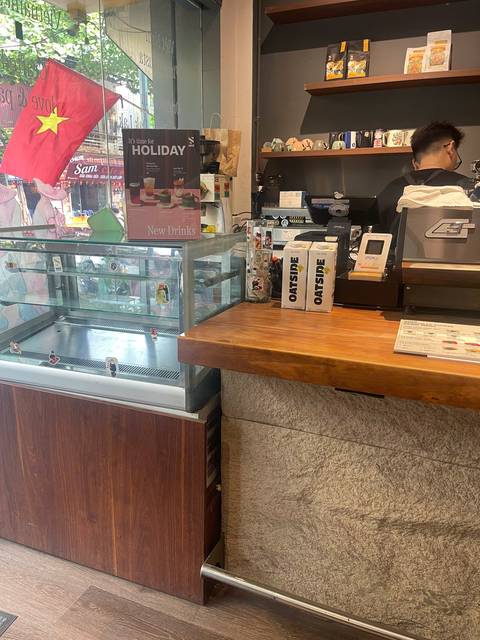 Countertop of a modern café showing refrigerated case and oat milk cartons; no clear travel context.