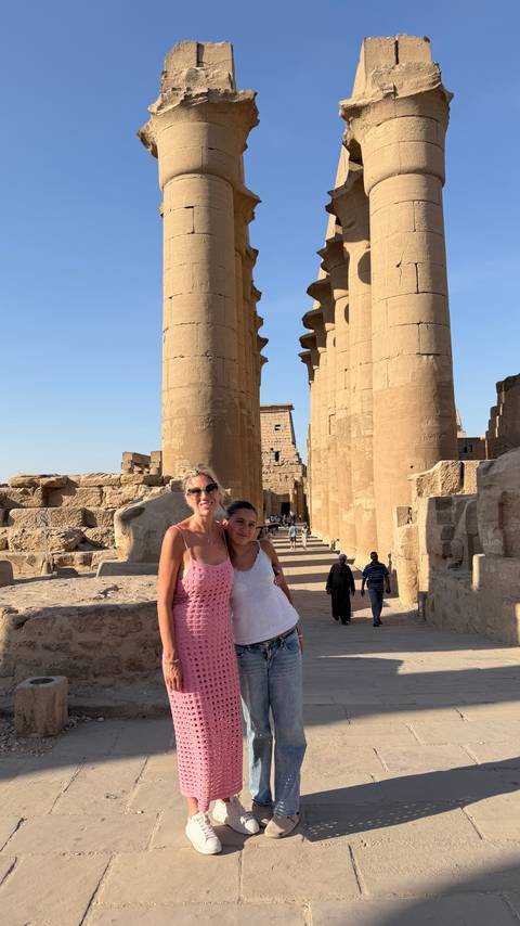 Smiling women pose among massive sandstone columns of Luxor Temple bathed in late-afternoon light.