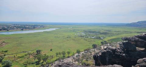 Expansive green wetland plain viewed from a rocky escarpment with distant village and river