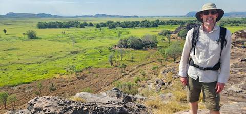Male hiker wearing a sunhat and backpack smiling at a scenic lookout over a broad wetland